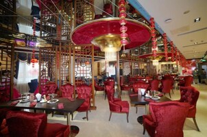 Un restaurante con sillas y mesas tapizadas de rojo, un candelabro grande y una decoración tradicional al estilo asiático.