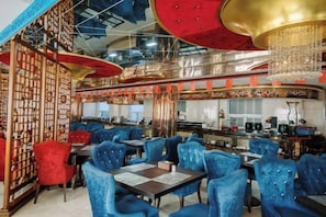 A restaurant with blue upholstered chairs, a red and gold decor, and a bar area. - Run Zeng Hotel (Dandong)