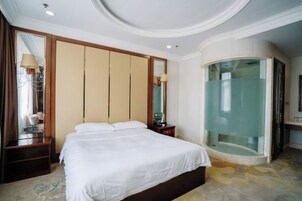 Habitación de hotel con cama, espejo, mesita de noche, ducha con mampara de vidrio y techo curvo.