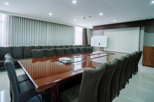 Un salón de conferencias con una larga mesa, sillas, una pizarra y una pantalla de proyección.