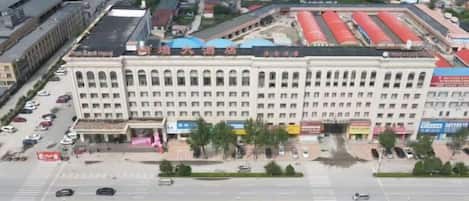 Un edificio de varios pisos con una entrada central, rodeado por un estacionamiento y una calle.