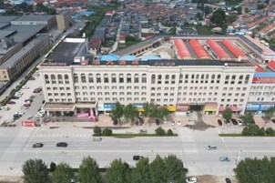 Un edificio de varios pisos con una entrada central, rodeado por un estacionamiento y una calle.