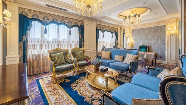 Un salon luxueux avec un canapé bleu, des fauteuils richement décorés, un lustre et une moquette à motifs.