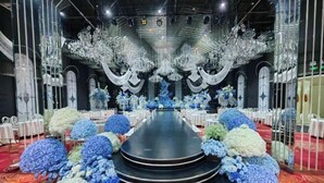 Une grande salle avec une scène centrale, des rangées de tables et des compositions florales.