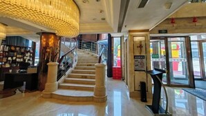 Un hall d’hôtel avec un escalier en marbre, un lustre et un comptoir d’accueil.