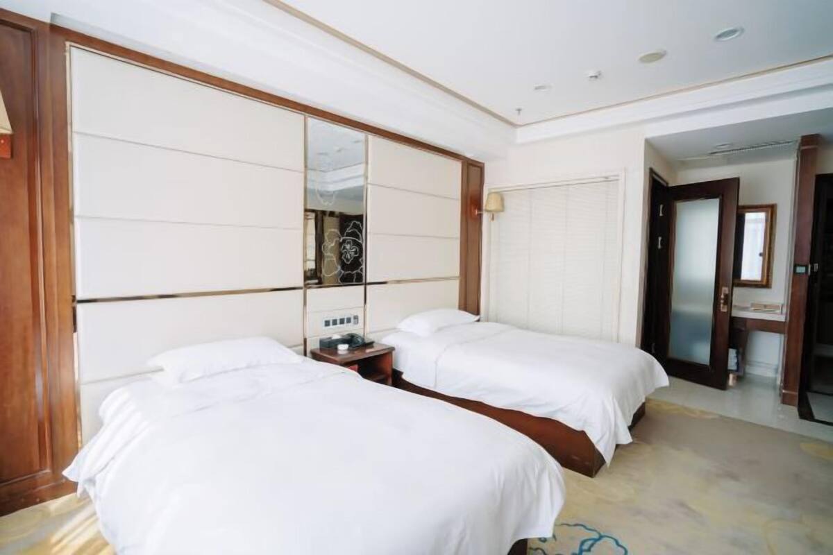 A hotel room with two beds, a large mirror, a nightstand, and a door leading to another room.