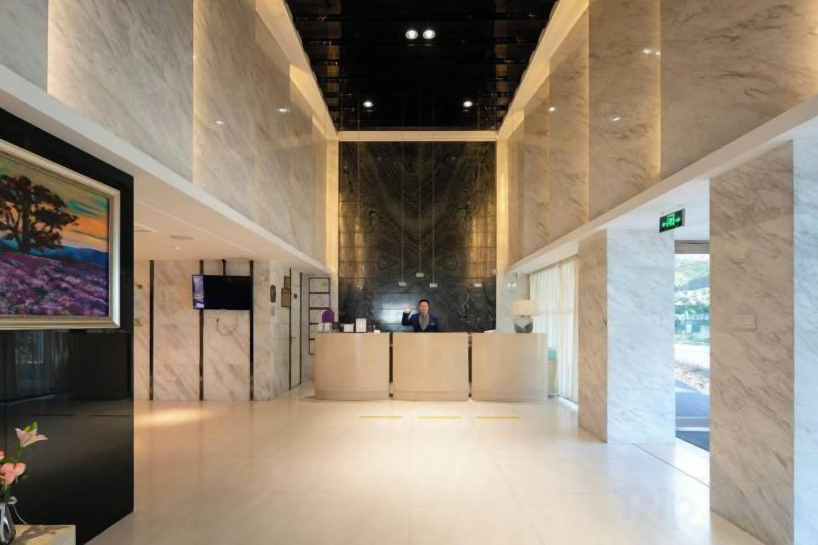 A hotel lobby with marble floors, a reception desk, and a large painting on the wall.