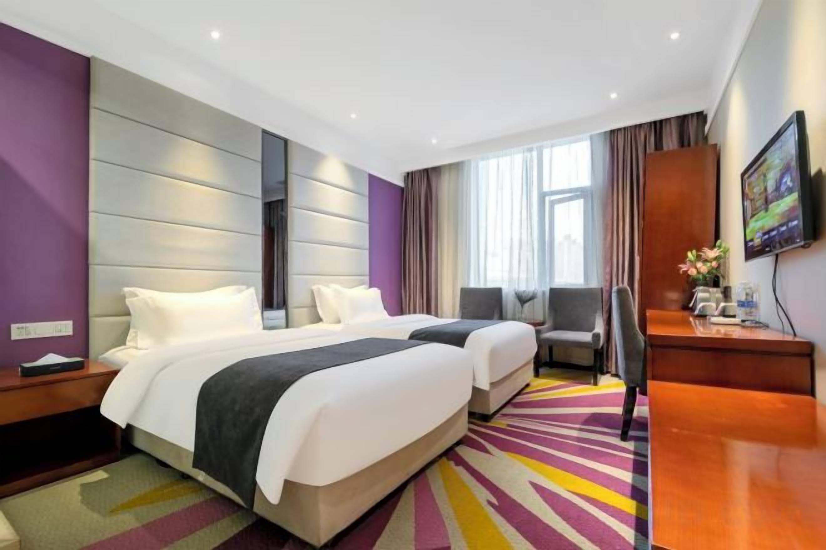A hotel room with two beds, a desk, a chair, and a television.