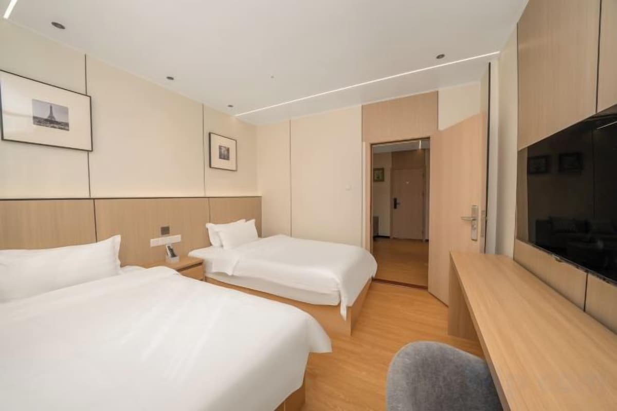 A hotel room with two beds, a desk, a TV, and a door leading to another room.