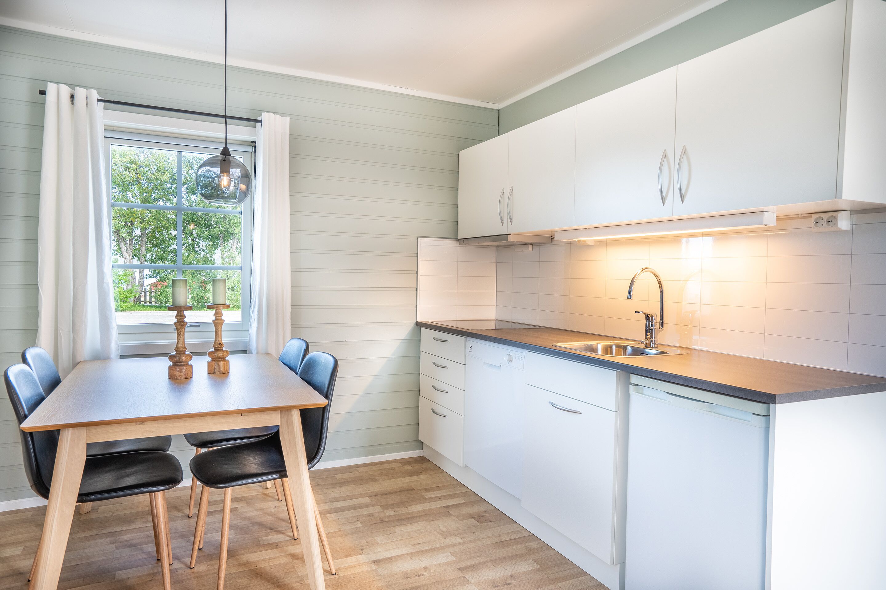 A modern kitchen with white cabinets, a wooden dining table, and a window with curtains.