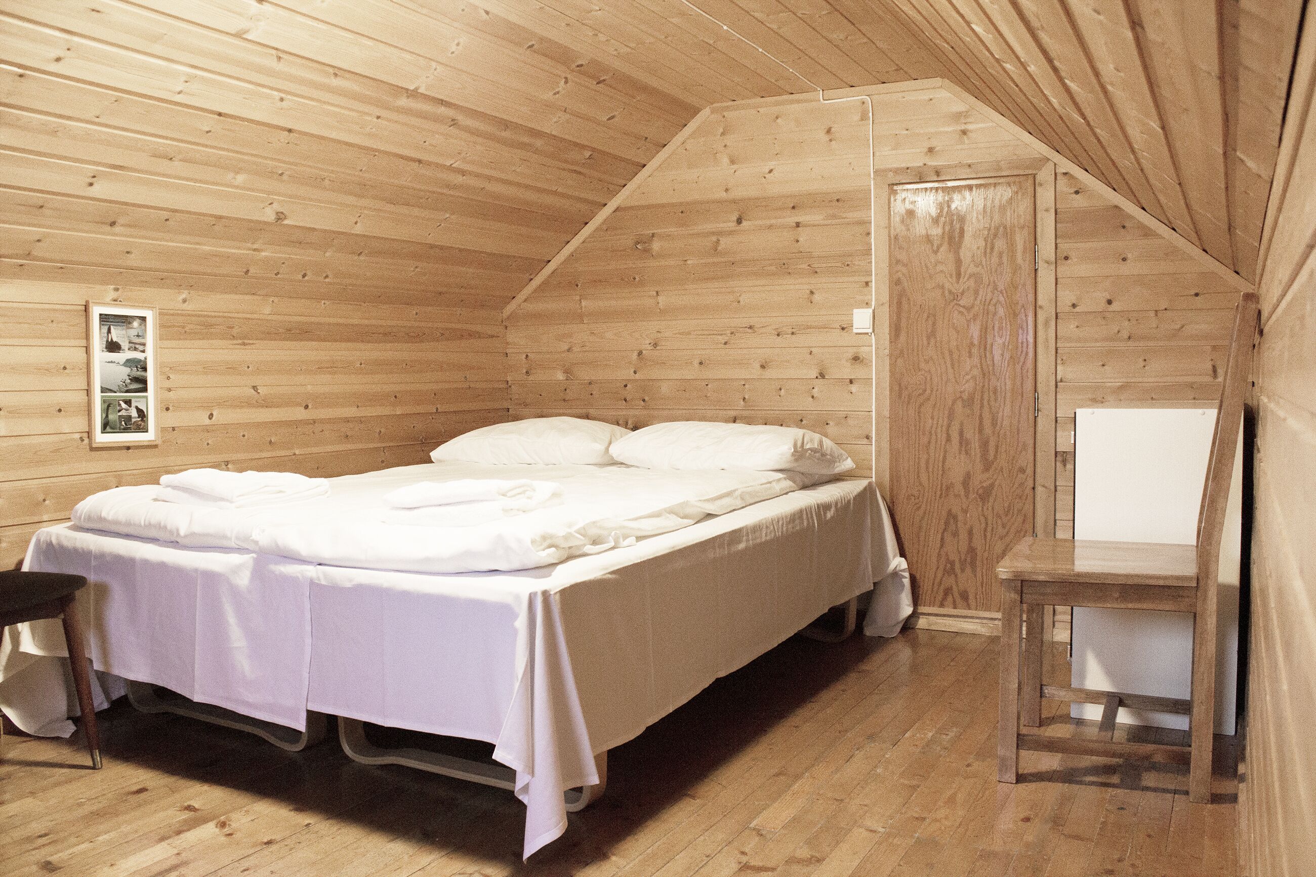 A wooden-paneled room with a bed, a small table, and a door.