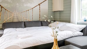 Una cama con sábanas blancas, cabecera gris y una obra de arte con un puente de cuerda sobre ella.