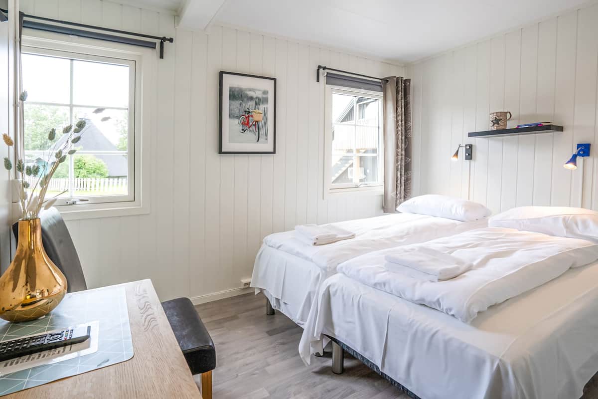 A bedroom with two beds, a desk with a vase, a framed picture, and a window with curtains.