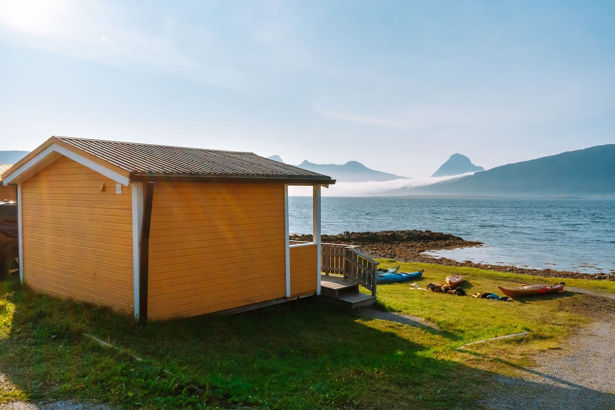 A wooden cabin by a lake with boats and a view of mountains.