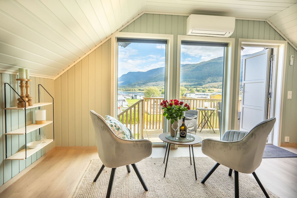 A balcony with two chairs, a table with a vase of flowers, and a view of a mountainous landscape.