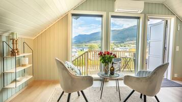 A balcony with two chairs, a table with a vase of flowers, and a view of a mountainous landscape.