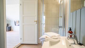 A bathroom with a white sink, a glass shower enclosure, and a door leading to a hallway.