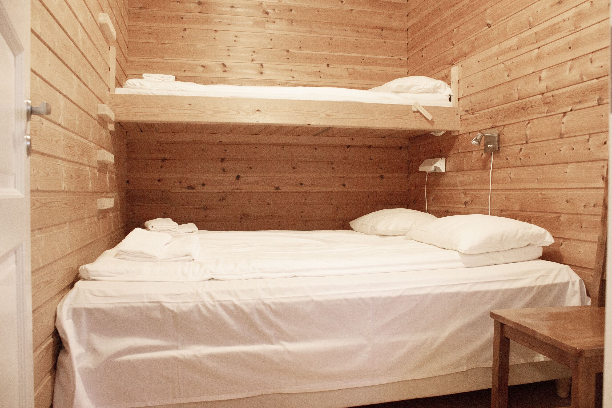 A small, wooden cabin-style room with a bunk bed, a single bed, and a small table.