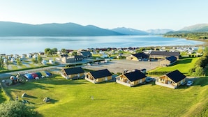 Un camping junto al lago con cabañas, vehículos recreativos y un amplio estacionamiento.