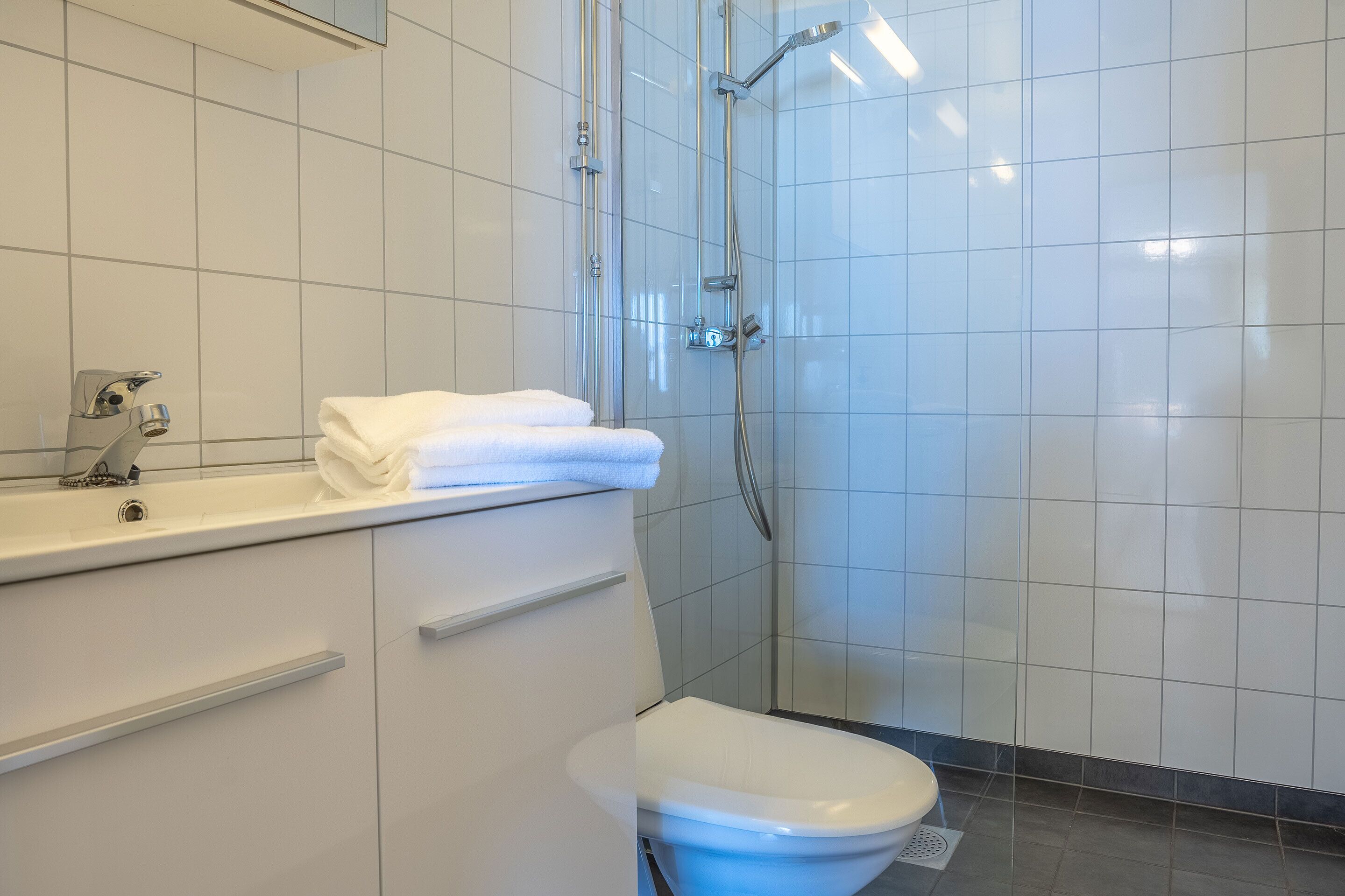 Un baño moderno con lavamanos, inodoro y zona de ducha blancos.
