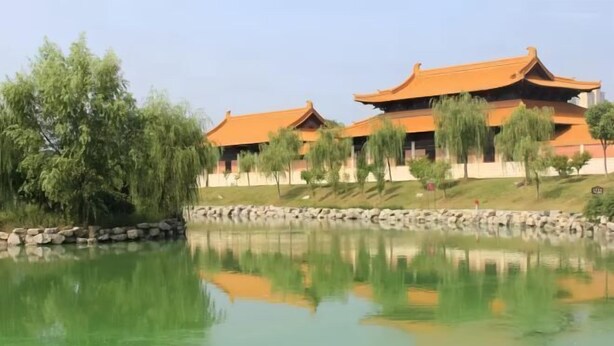 Ein traditionelles Gebäude mit einem Teich davor, umgeben von Bäumen und einer Steinmauer.