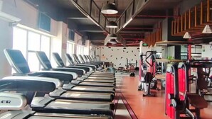 Ein Fitnessraum mit Laufbändern an einer Wand, Krafttrainingsgeräten und einer roten Trainingsbank.