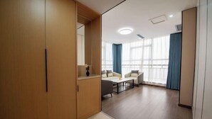 Ein modernes Zimmer mit Holzschrank, einer Couch, einem Couchtisch und großen Fenstern mit Vorhängen.