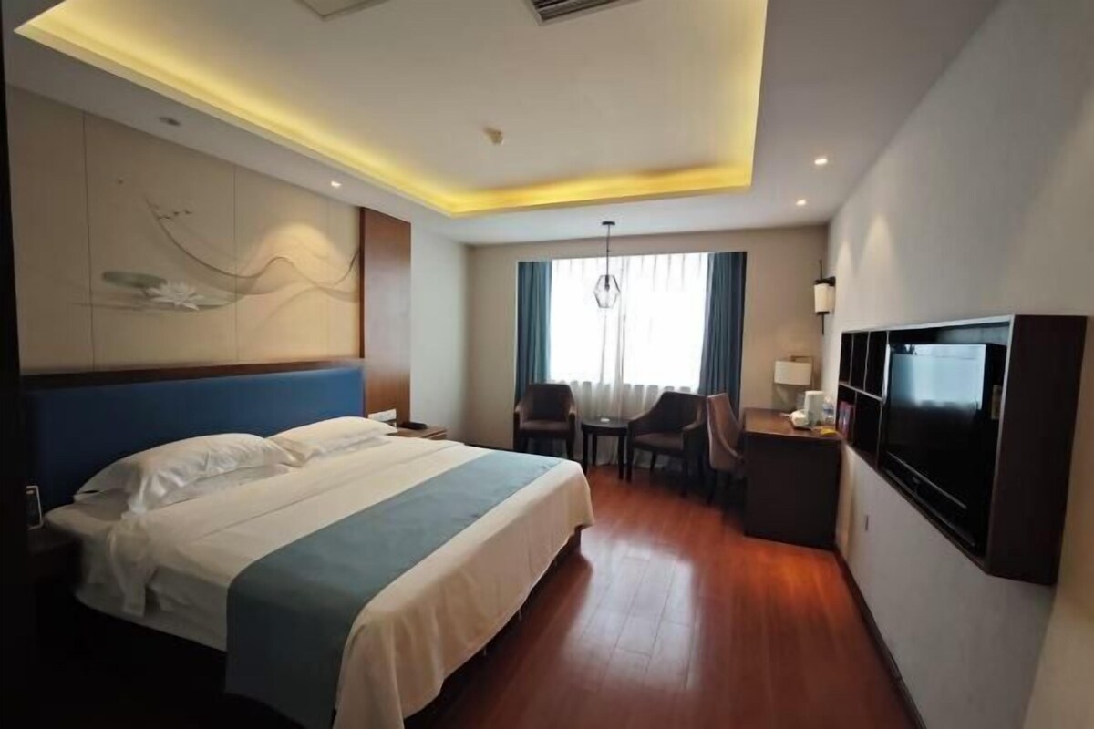 Una habitación de hotel con cama, escritorio, silla, televisión y ventana con cortinas.