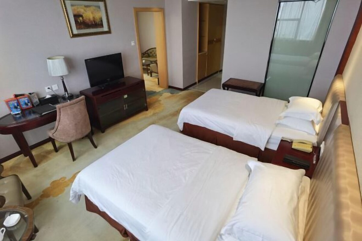 Una habitación de hotel con dos camas, un escritorio con televisor, una silla y un armario.