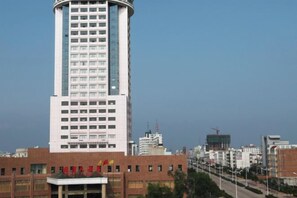 A tall, modern building with a cylindrical section, surrounded by other buildings and a clear sky.