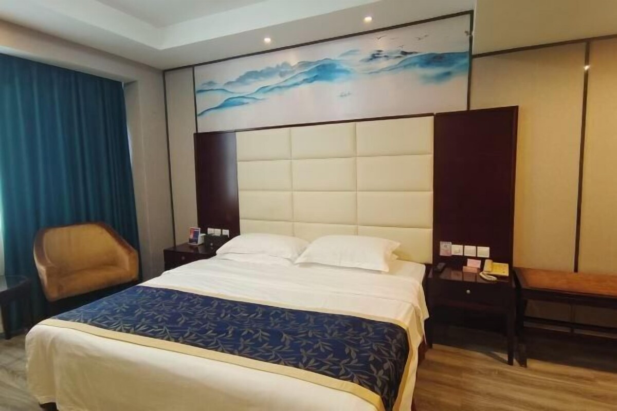 Una habitación de hotel con una cama grande, un cabecero con una obra de arte azul, un banco de madera y un escritorio con una lámpara.