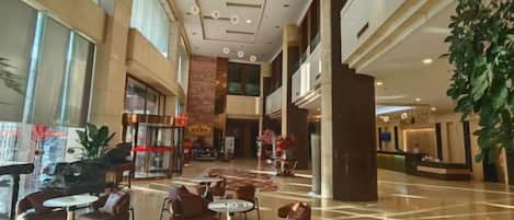 Un espacioso vestíbulo de hotel con varias zonas de estar, una recepción y una planta grande.