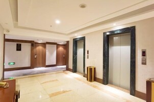 A hotel lobby with a marble floor, wooden doors, and two elevators.