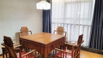 A wooden dining table with six chairs, a chandelier, and large windows with sheer curtains.