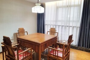 Una mesa de madera para comer con seis sillas, una araña y ventanas grandes con cortinas translúcidas.