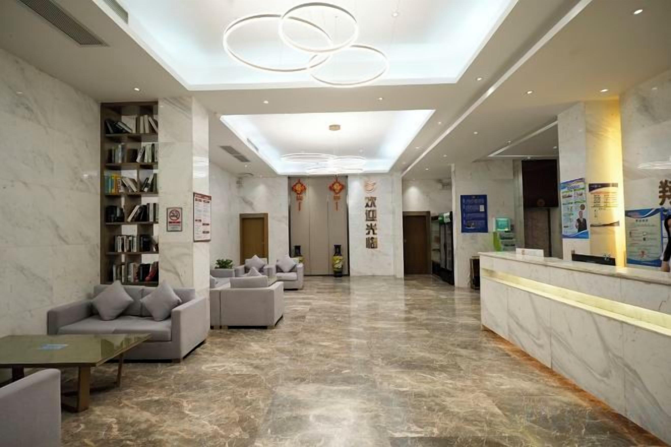 Un vestíbulo de hotel con mostrador de recepción, zona de estar y estantería.