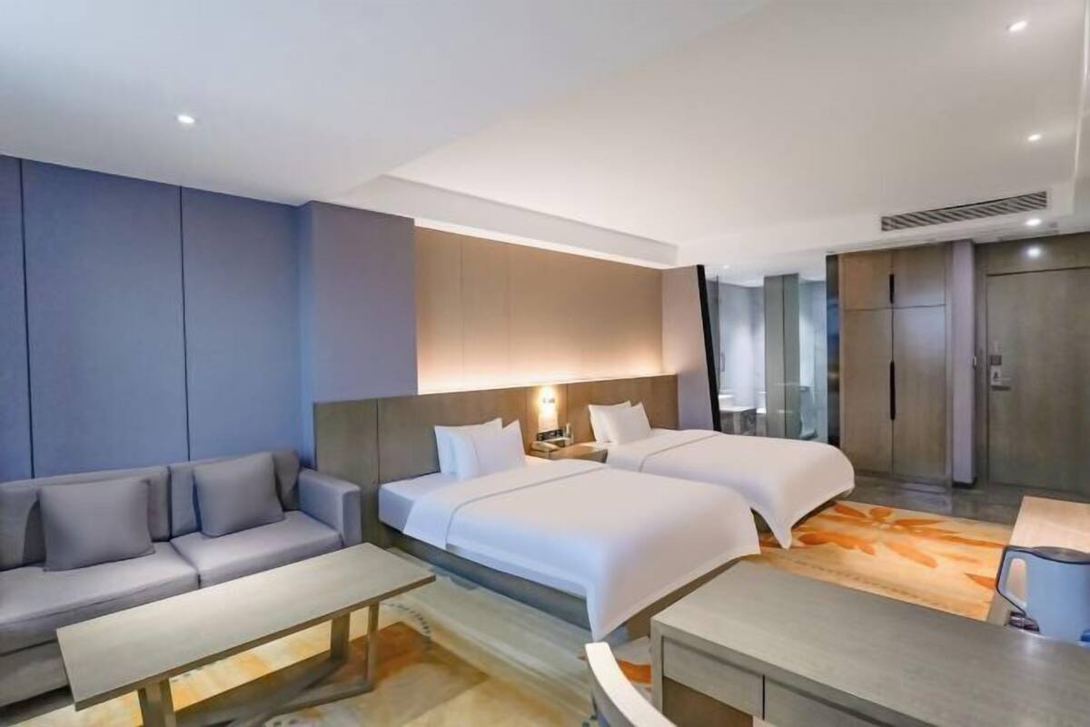 Een moderne hotelkamer met twee bedden, een bank, een kleine tafel en een kitchenette.