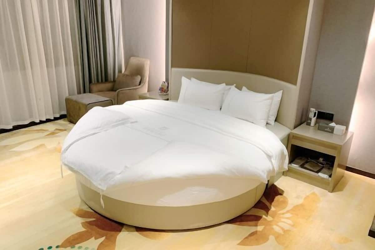 Een hotelkamer met een rond bed, een stoel, een nachtkastje en een raam met gordijnen.