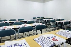 Un salón de conferencias con filas de mesas y sillas, algunas con documentos y tarjetas de identificación.