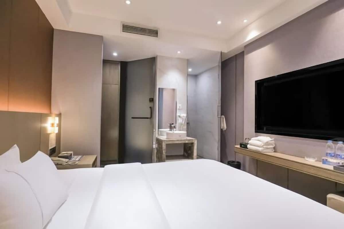 Een hotelkamer met een bed, een nachtkastje met een telefoon, een bureau met een televisie, een badkamer met een wastafel en een spiegel.