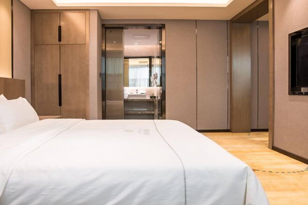 Een hotelkamer met een bed, een televisie, een kledingkast en een badkamer die zichtbaar is door een glazen deur.