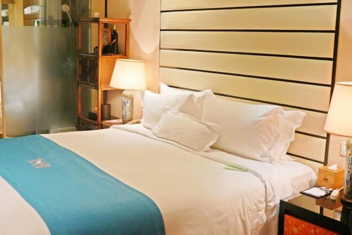 Una habitación de hotel con una cama, una mesita de noche, una lámpara y un espejo.