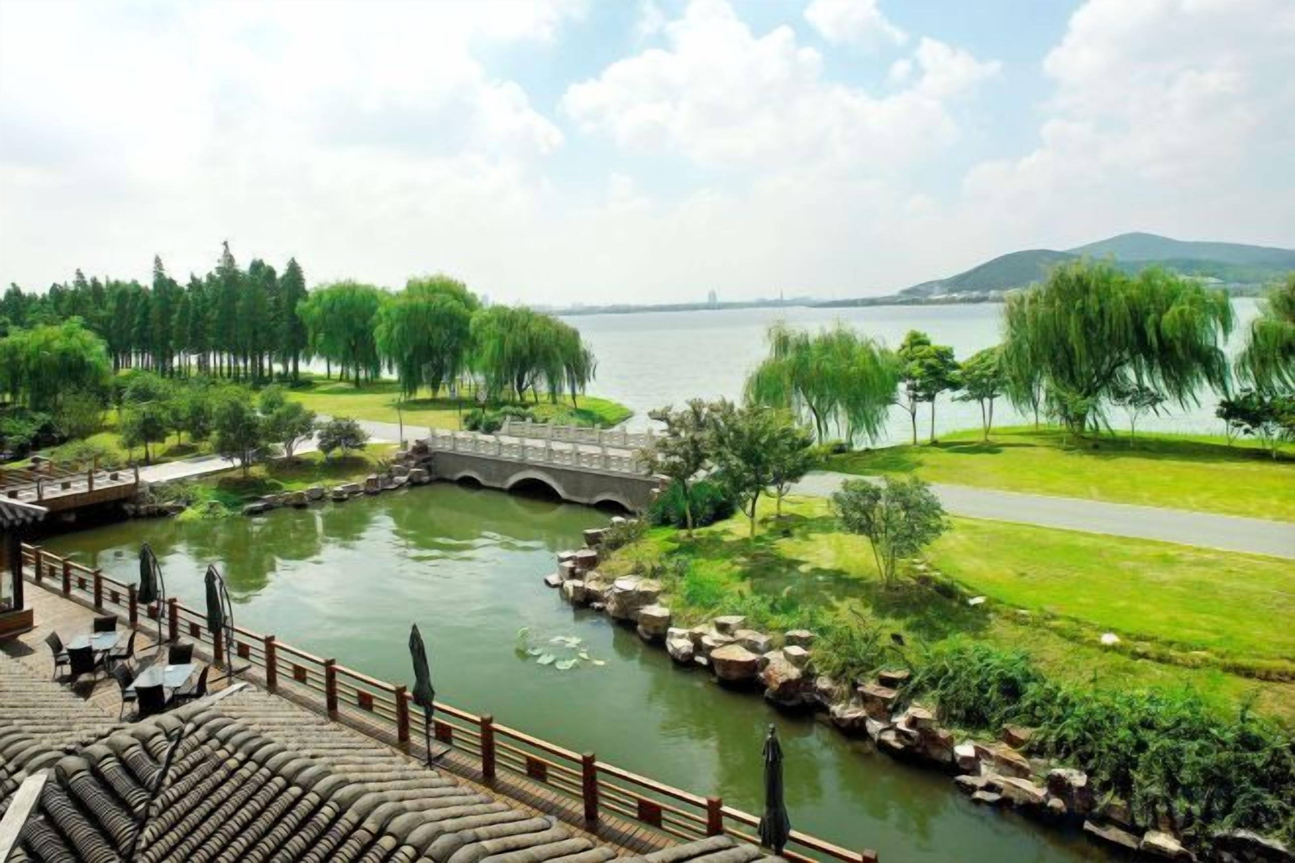 A riverside view with a bridge, grassy areas, and a paved path.