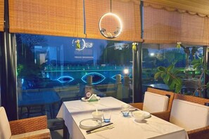 A dining area with a table set for two, a view of a water feature outside, and a hanging light fixture. - 1881 Peninsula Hotel (Wuxi)