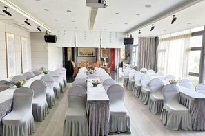 A conference room with long tables, chairs, and a stage. - 1881 Peninsula Hotel (Wuxi)