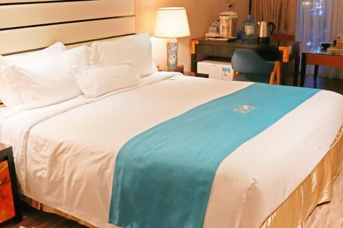 Una habitación de hotel con cama, escritorio, silla, lámpara y cafetera.