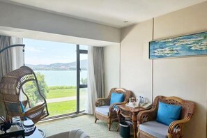 A room with a view of a lake, wicker chairs, a sofa with blue cushions, and a painting on the wall.