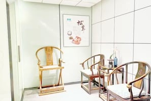 A room with a traditional chair, a small table with a vase, and a poster on the wall. - 1881 Peninsula Hotel (Wuxi)