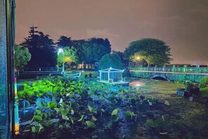 Un parque de noche con un pabellón, un estanque con nenúfares y un puente.