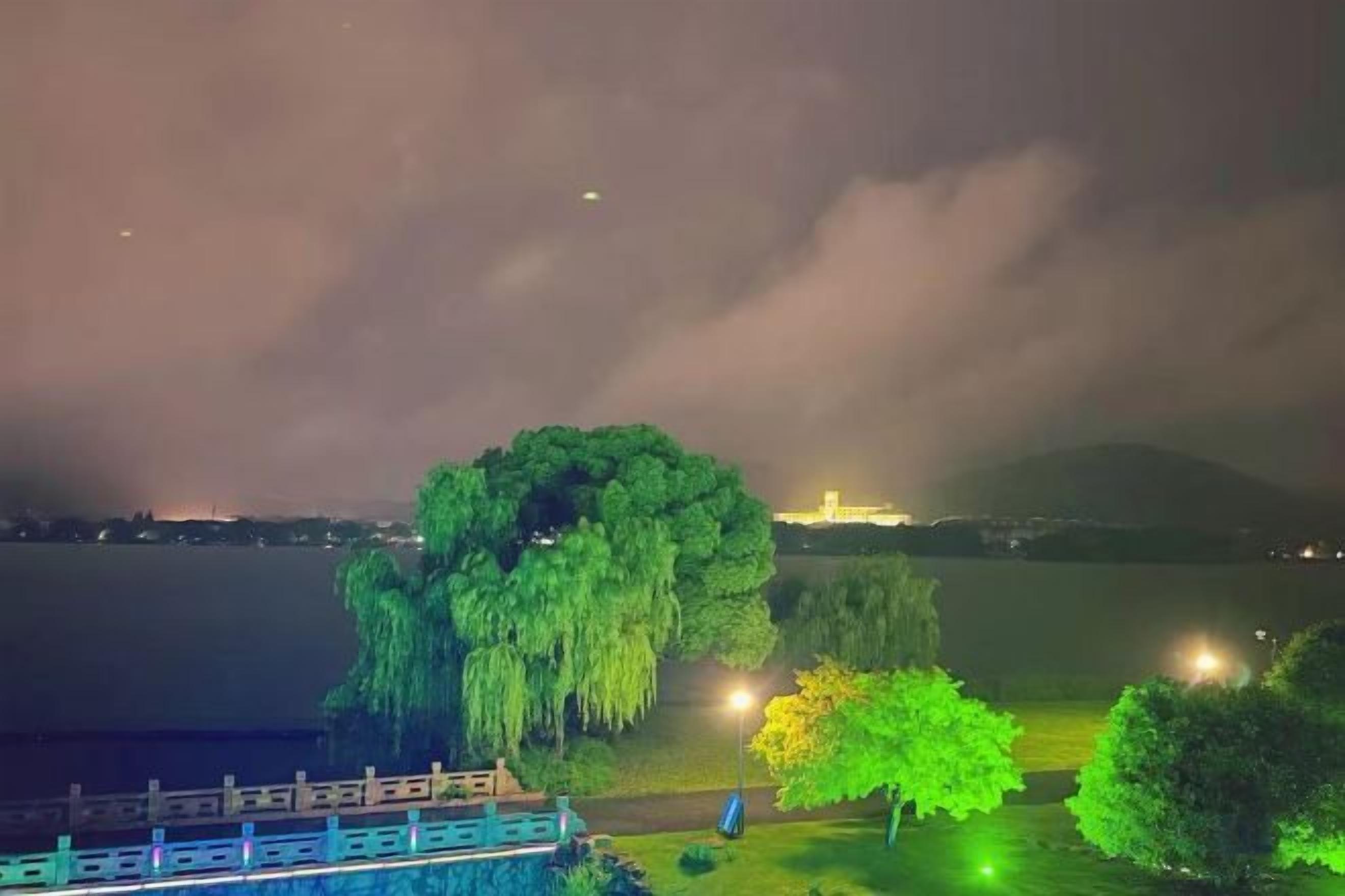 A nighttime view of a lake with a bridge, trees, and a distant mountain.